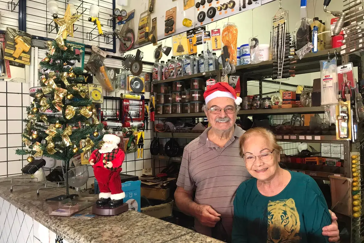 Os fundadores atrás do balcão da loja, com as prateleiras de ferramentas ao fundo